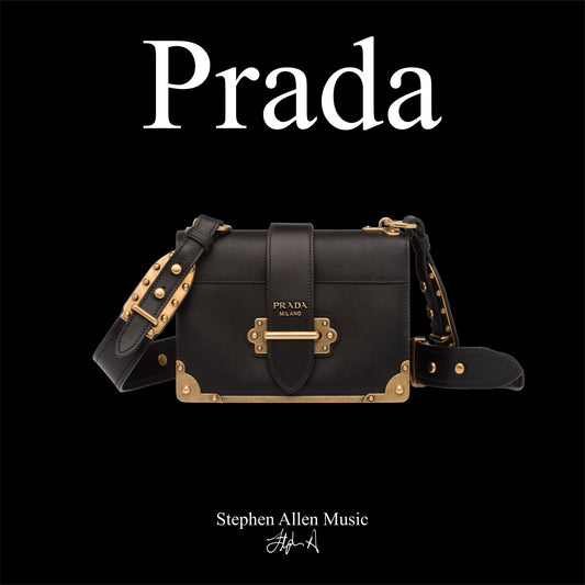 Black Prada handbag with gold accents on a black background, featuring the Prada logo. Stephen Allen Music