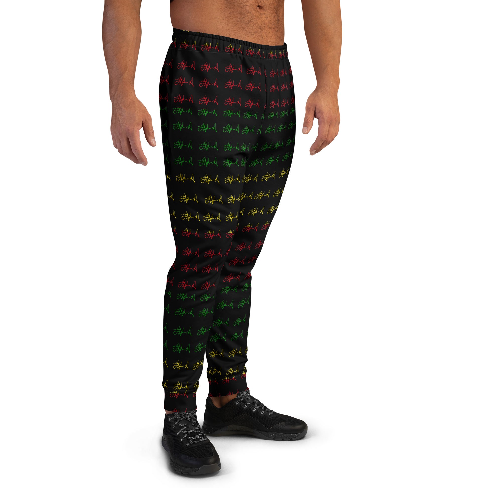 A model wearing black jogger-style pants with a repeating red, green, and yellow graphic pattern, paired with black sneakers, shown against a plain white background. Stephen Allen Music